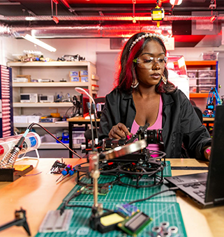 student seated in front of soldering project with laptop in a  workspace setting