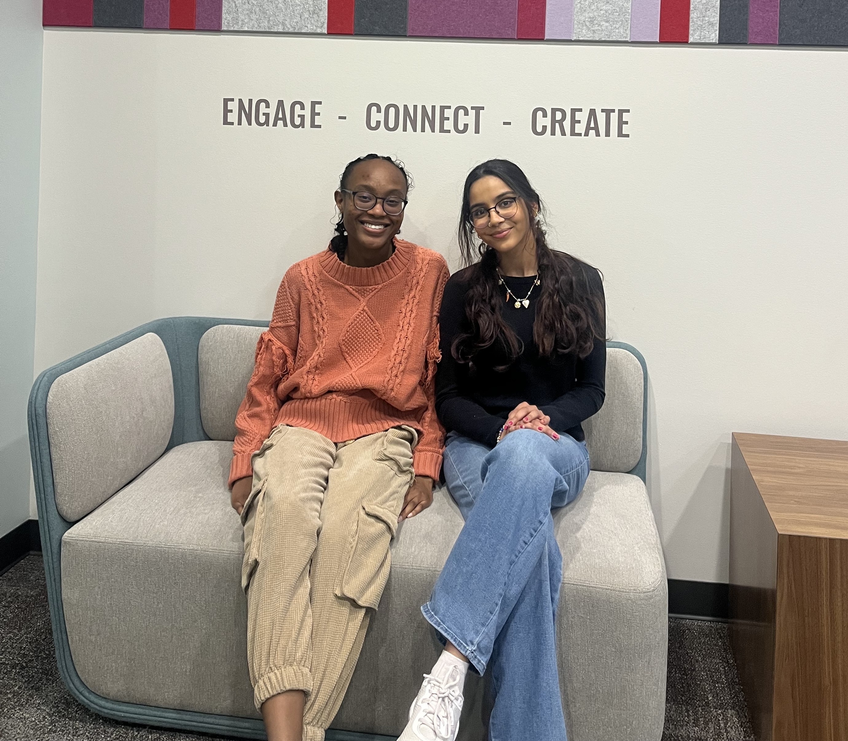 two peer research consults sitting under wall sign that says "engage, connect, create"
