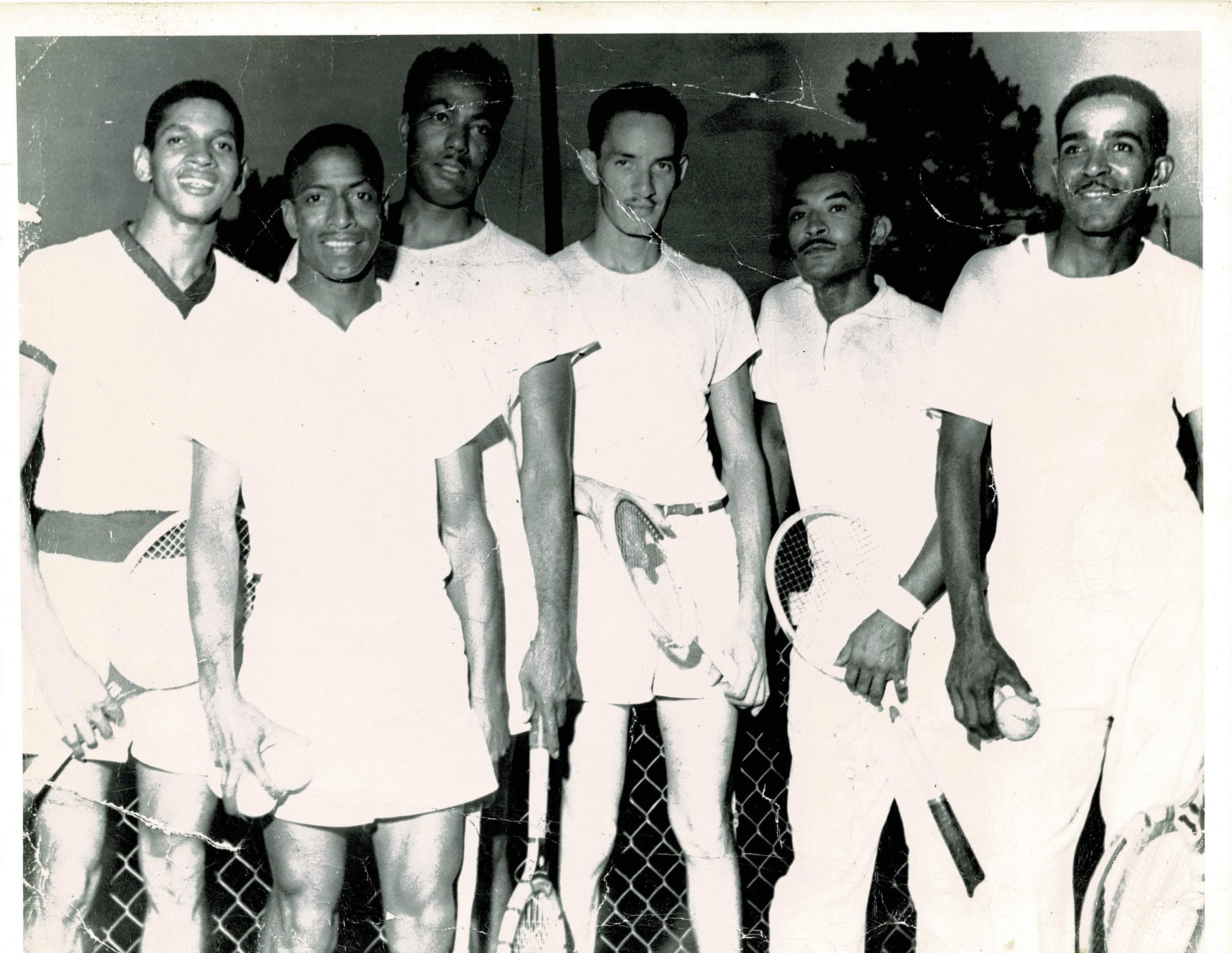 A group of male tennis players pose with their rackets, smiling