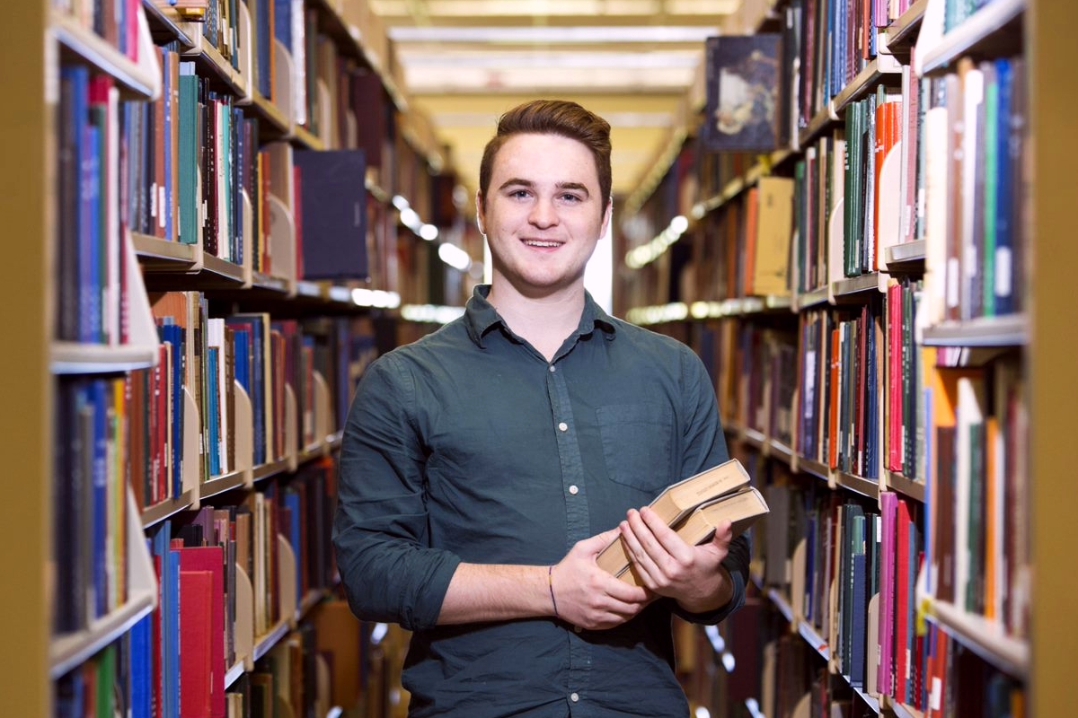 male student standing in book stacks at Main Library