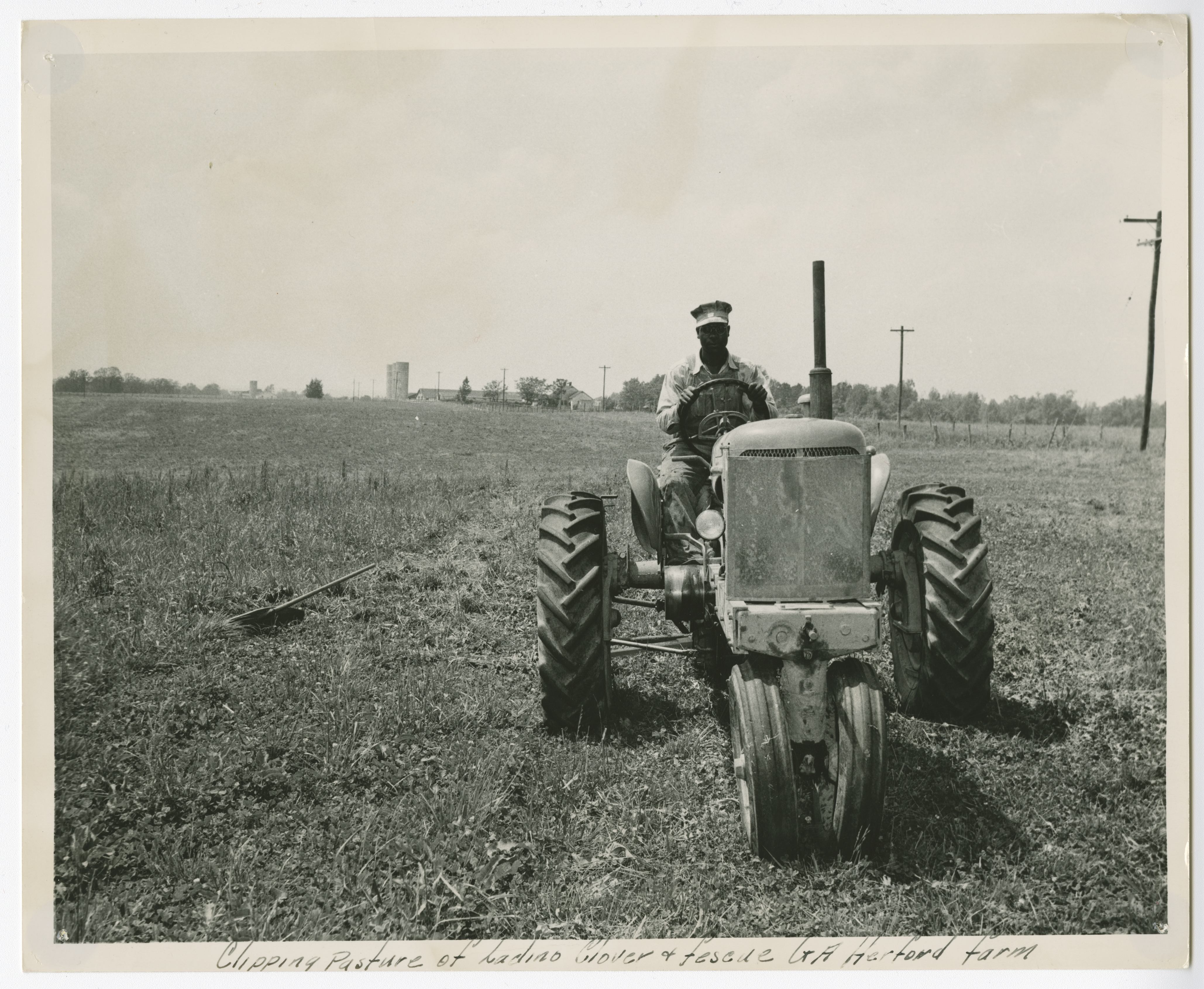 African-American agricultural worker riding a tractor and clipping pasture 