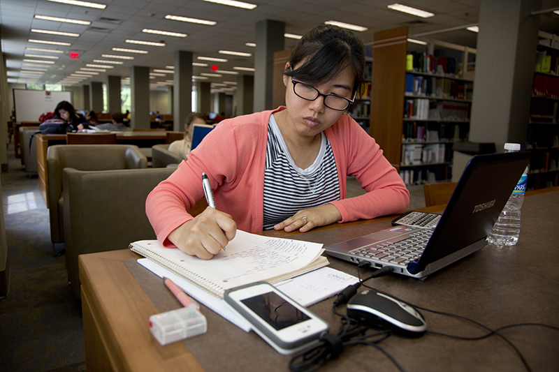 A student writes at a desk in the library