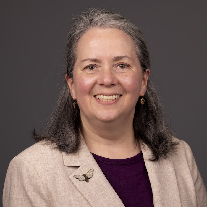 woman with hair pulled back smiling brown eyes and beige blazer