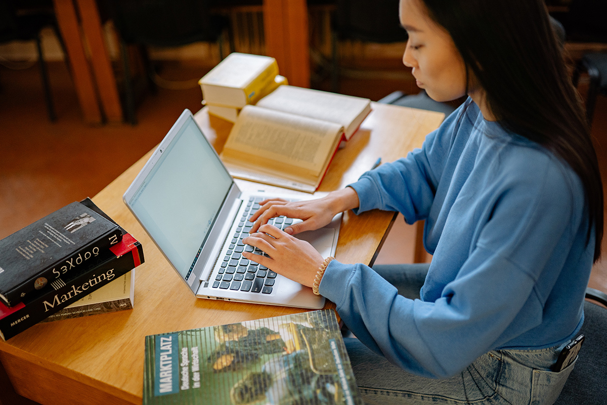 Student sitting at laptop, surrounded by books