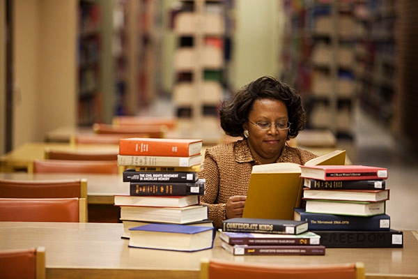 female faculty member with stack of books at table in Main Library