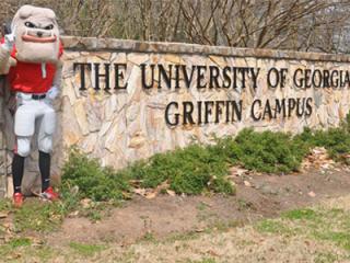 Mascot "Hairy Dawg" standing beside a stone wall that read "The University of Georgia Griffin Campus"