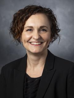 Curly haired woman wearing a black shirt and black blazer