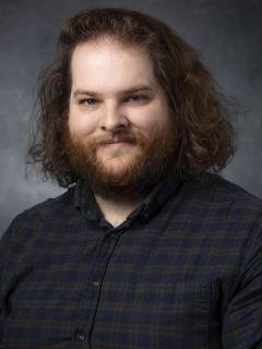 Man in plaid shirt with beard and shoulder length curly brown hair