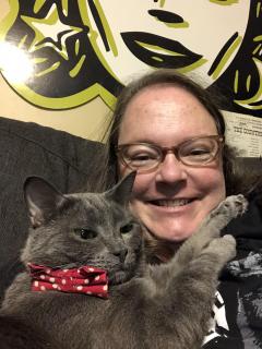 Woman with long brown hair and glasses with a grey cat wearing a bow tie