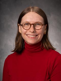 Woman with shoulder length hair, glasses, and red turtleneck.