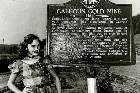 A woman poses for a picture in front of the Calhoun Gold Mine historical marker in Dahlonega.