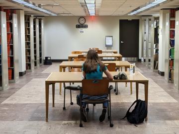 A young woman sits at a large table in an open area between book stacks